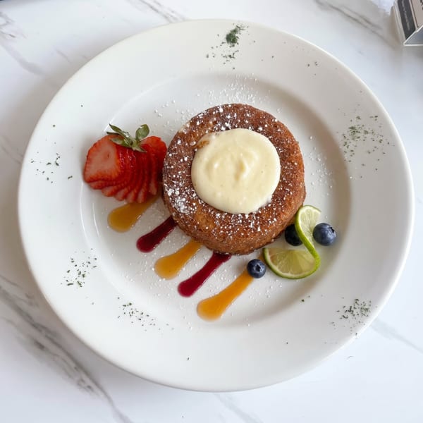A round dessert with cream, powdered sugar, sliced strawberries, blueberries, lime, and colorful sauces.