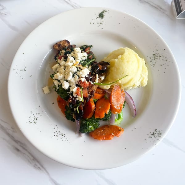 A white plate with mashed potatoes, roasted vegetables, and a feta-topped chicken dish.