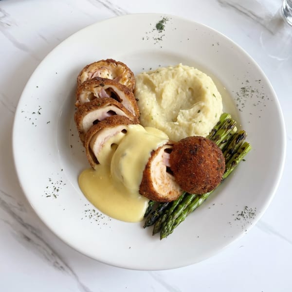 Chicken cordon bleu with mashed potatoes, asparagus, and a creamy yellow sauce on a white plate.